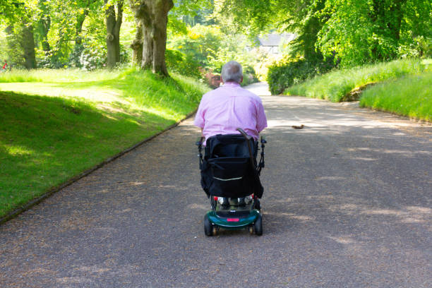 Middle aged man on mobility scooter, rear view enjoying riding his scooter outdoors and having access to the outdoors despite his disability.