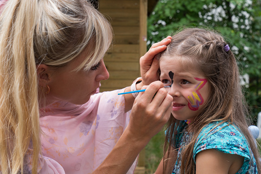 The girl draws a picture on the face of a little girl.
The face of a little girl with a pattern on her face. An artist paints a butterfly on a child's face