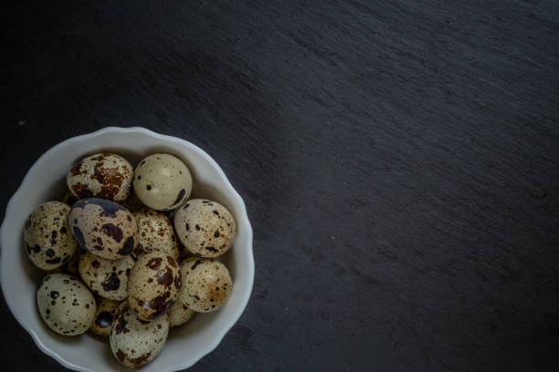 istock Fresh quail eggs in white plate on black stone, selective focus 2109698589
