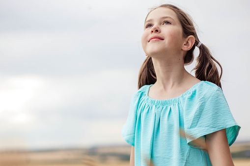 Portrait of adorable girl looking up against sky background.