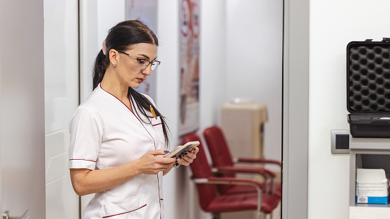 At the modern ENT clinic, female Caucasian nurse use app on mobile phone, to adjust and prepare medical instrument and equipments for an medical exam