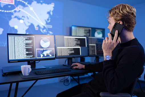 Cyber security analyst in a cyber security operations center (SOC) in a important phone call. Multiple screens showing map, incident logs and alert data.