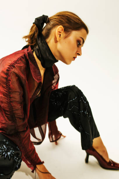 Side view of beautiful young woman with short hair looking at camera and putting on translucent trendy jacket against white background