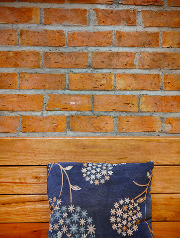 Hand embroidered fabric cushions on wooden bench with red brick wall as background, rest relax corner, contrast color design, home decoration