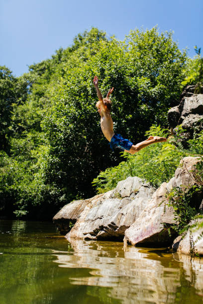 Boy having fun on his summer vacation , jumping from a cliff in the river