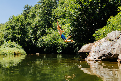 Boy having fun on his summer vacation , jumping from a cliff in the river