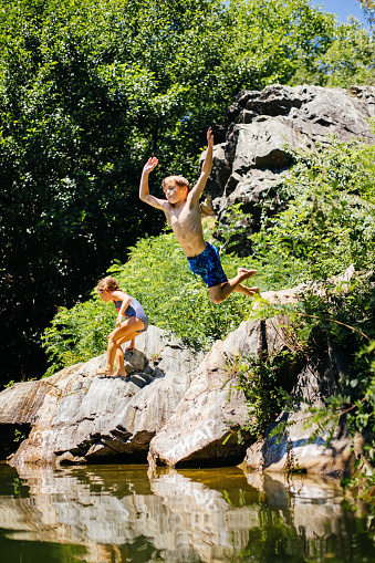 Happy children swim in the lake in the summer. The concept of summer holidays, weekends, holidays. Active lifestyle, outdoor entertainment. A hot summer day. Jump into the water and flying splashes