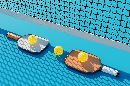 Two pickleball rackets and balls lie in a row near the net on the court. 3d rendering