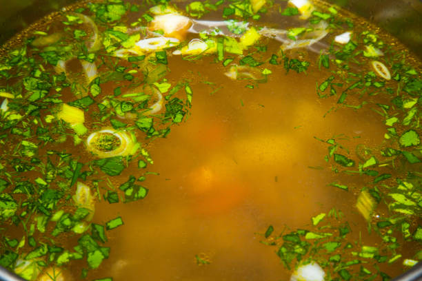Soup with meatballs, vegetables, herbs and egg in a pan close-up.