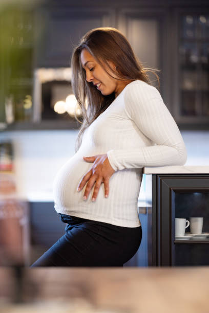 istock Expectant Smiling Mother Touching Her Pregnant Belly in the Kitchen 2110030262