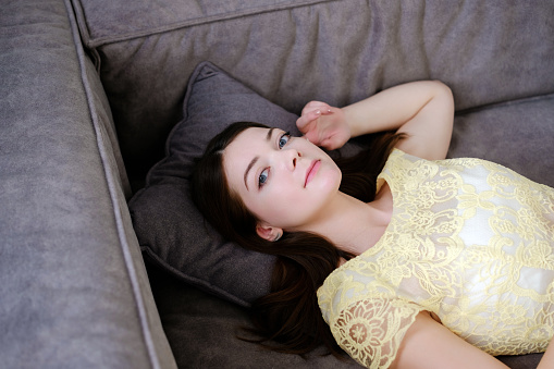 a pretty young brunette model girl lies in a yellow dress on the sofa resting. relaxation and enjoyment. girl posing in the studio lying on the sofa. portrait photo