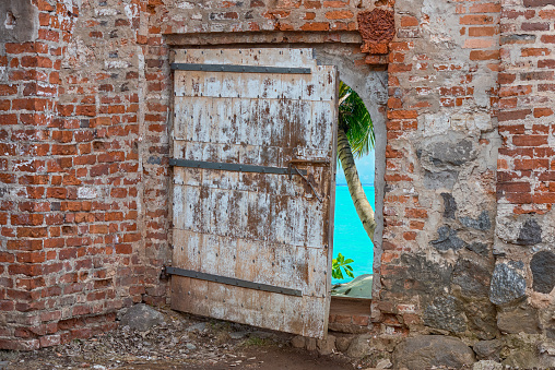 A half-open wooden door in a brick wall overlooking the seashore. Beautiful seashore through the gap in the door.