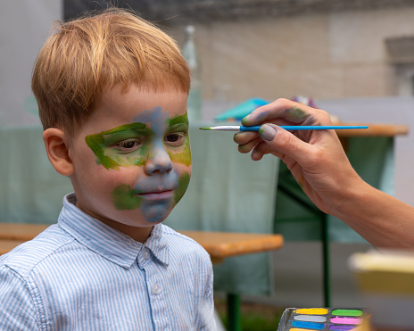 The girl draws a picture on the face of a little boy.
The face of a little boy with a pattern on his face. The artist draws a picture of a kind, green dragon on the face of a child