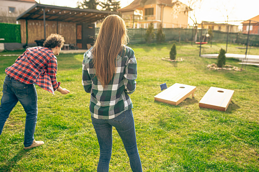 Couple playing cornhole game outdoor on sunny summer day.