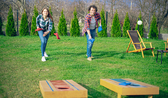 Couple playing cornhole game outdoor on sunny summer day.