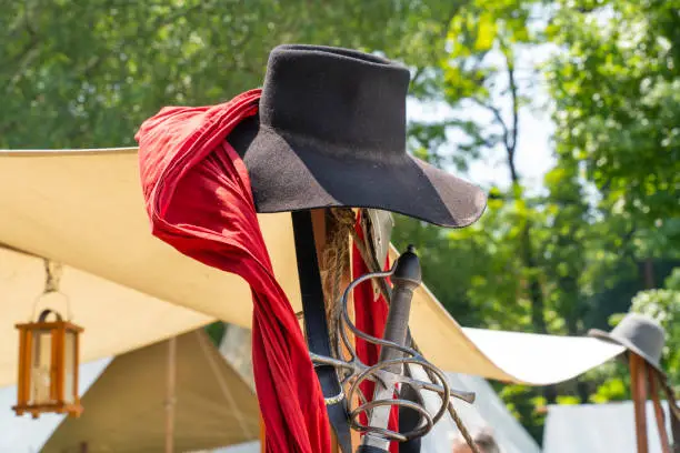 A black felt hat and the hilt of a medieval sword suspended in a military camp