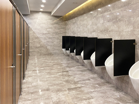 Modern and clean inside of public restroom, urinals and toilets with ceramics tile flooring and wall