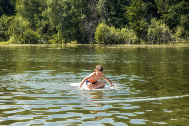 Persistent boy sailing on handmade raft overcoming efforts on river during sunny summer day concept happy childhood