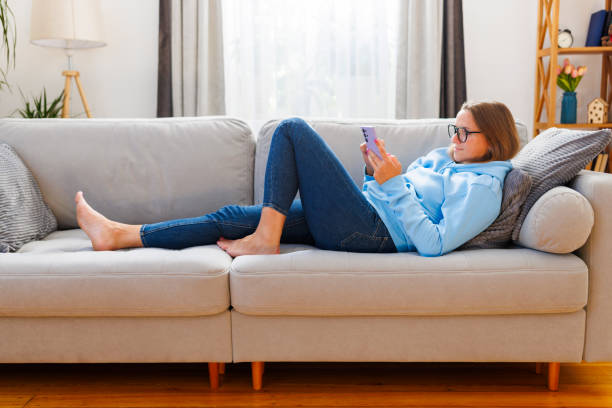 istock Relaxed woman lounging on a sofa with a smartphone 2110193296
