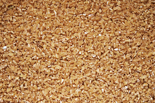 Background texture of fine ground brown bulgur made from cracked durum wheat or cereal groats rich in protein and dietary fiber for a healthy whole grain ingredient