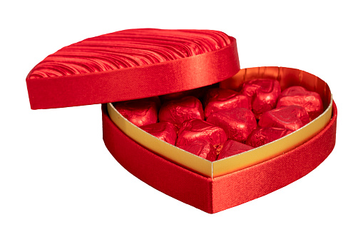 Top view of a opened chocolate box with a red ribbon surrounded by two red roses, a champagne cork, two hearts shape and a greeting card. All the objects are at the top of the image leaving a useful copy space at the lower side on a white background.