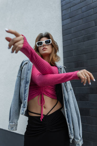 fashionable beautiful cool vogue dancer girl with stylish white sunglasses in fashionable denim bright urban outfit dancing near the black brick wall on the street. pretty woman - vogue dancing - fotografias e filmes do acervo