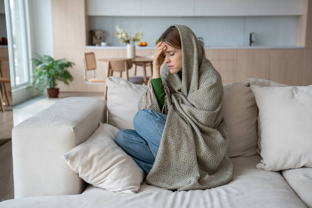 istock Suffering from pain, terrible headache, ill woman sitting on sofa covered in plaid, feeling cold 2110275708