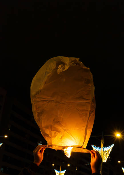 foreground, human hands release a Chinese lantern of light into the dark sky