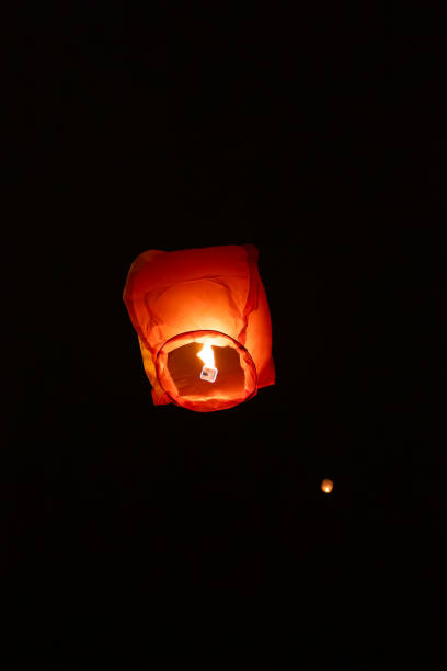 istock A single glowing orange sky lantern rises against a dark night background, surrounded by faint lights of other lanterns. 2110321681
