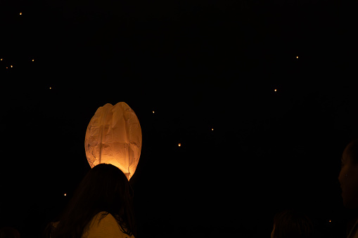 people release a lantern into the dark sky in the background more lanterns flying.