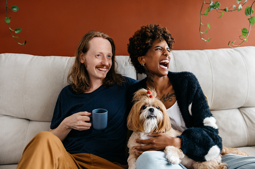 A comfortable and loving atmosphere as a couple laughing together and sharing quality time with their pet dog. Cuddling and enjoying a warm drink, showcasing a serene and homely vibe.