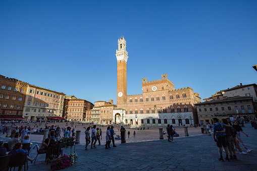 SIENA, ITALY - May, 2022: cityscape. View of famous Bell tower of the Palazzo Pubblico at the Piazzo del Campo at sunset time in Siena, Italy.