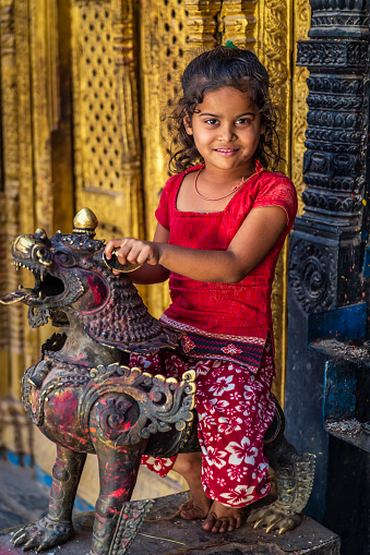 Portrait of little Nepali girl sitting in an ancient temple in Bhaktapur. Bhaktapur is an ancient town in the Kathmandu Valley and is listed as a World Heritage Site by UNESCO for its rich culture, temples, and wood, metal and stone artwork.