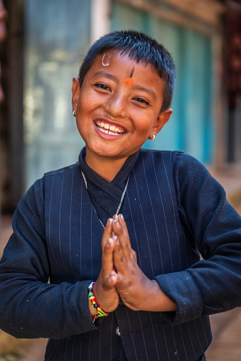Young Nepali boy saying namaste in Bhaktapur. Bhaktapur is an ancient town in the Kathmandu Valley and is listed as a World Heritage Site by UNESCO for its rich culture, temples, and wood, metal and stone artwork.