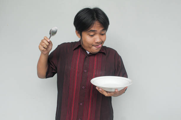 istock Asian young man looking to empty eating plate and holding spoon with funny expression. 2110421192