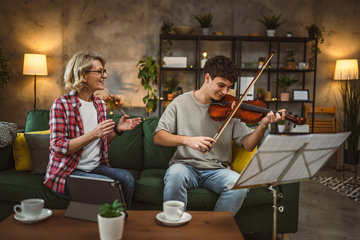 Young man learn how to play violin under instruction of mature woman female professor tutor at home take private class