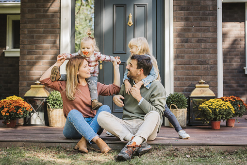 Young family with two kids having fun in front of there house. Porch is decorated with flowers.