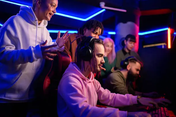 Professional eSports gamer diverse team playing online strategy video game on a computer in a internet cafe or cybersport gaming lounge. Group of gaming lovers spending time together in a gameroom.