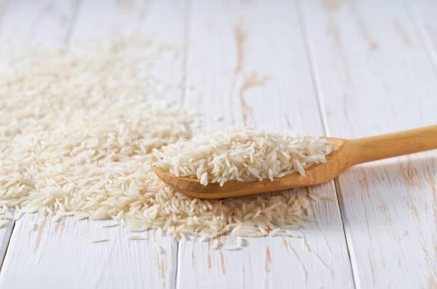 istock Raw long rice basmati crumble from a wooden spoon on a white wooden table. 2110645236