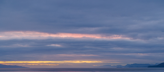 Colorful and dynamic cloudscape over a bay with islands and mountain ranges in Alaska, USA