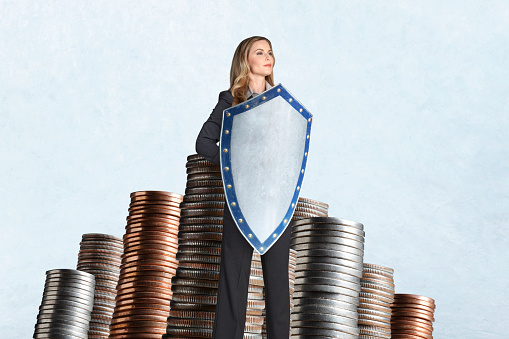 A woman holding a medieval shield stands confidently and protectively in front of several stacks of coins.