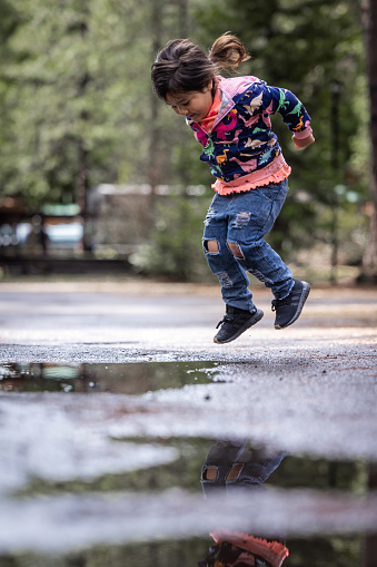 A young girl is jumping in a puddle of water. Concept of joy and playfulness, as the girl is having fun while splashing in the water. The puddle reflects the surrounding environment