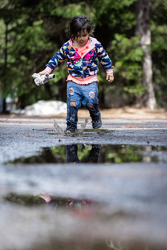A young girl is playing in the rain, splashing in puddles. The scene is playful and joyful, with the girl enjoying the moment and the wet environment