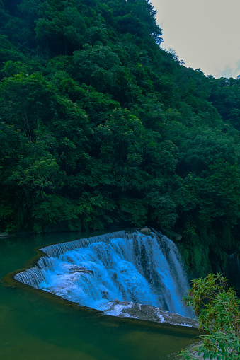 The cliff of Shifen waterfall in Taiwan is lined with dense greenery, creating a beautiful scene in the summer sky.