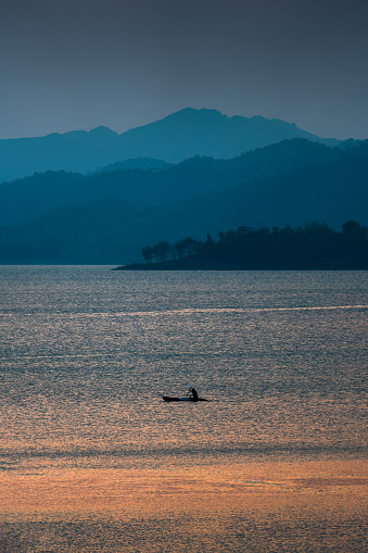 Colorful sunset view of the Kaeng Krachan reservoir with fishing boat and tourist rowing canoe at Phetchaburi, Thailand