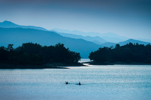 Colorful blue scene of the Kaeng Krachan reservoir with fishing boat and tourist rowing canoe at Phetchaburi, Thailand