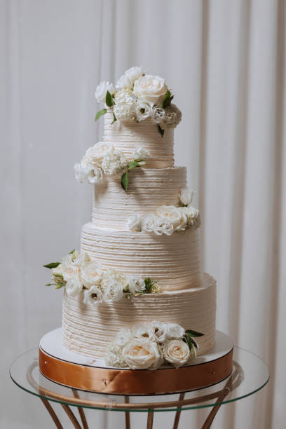 istock A large luxurious multi-tiered wedding cake is decorated with fresh white rose flowers in the banquet hall. Wedding dessert under the evening light. Wedding decor. 2110772711