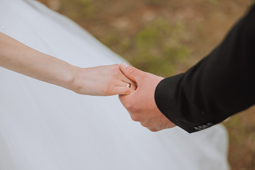 The groom holds the bride's hand. Cropped photo. Groom in a black suit. Details