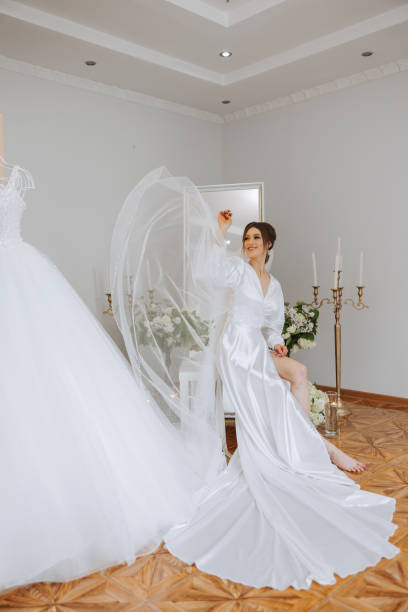 istock A beautiful brunette bride is getting ready for the wedding in a beautiful boudoir style outfit sitting on a chair among fresh flowers and stylish candlesticks. Wedding portrait, photo. 2110774890