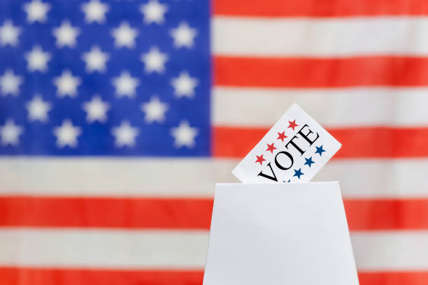 Ballot being cast with US flag background. Ballot reads 'Vote,' encouraging citizens to participate in voting